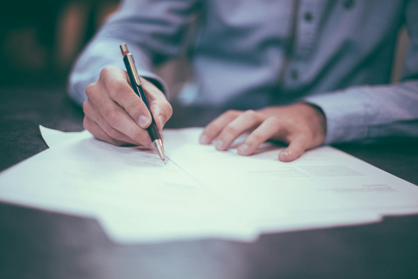A person signing paperwork with a pen at a desk, illustrating the dealership negotiation process.