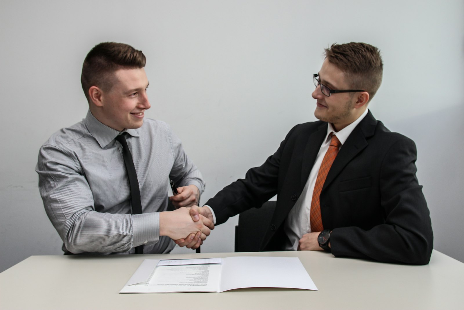 Two people shaking hands over paperwork at a desk, representing a car-buying deal being closed.